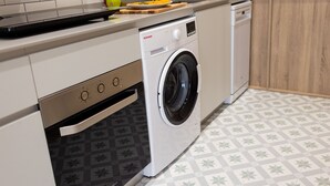 Cuina compacta amb rentadora integrada, microones i taula de tall de fusta amb fruita.