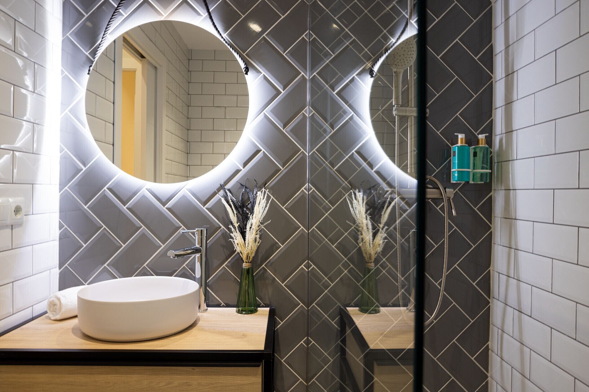 Un baño moderno con un espejo redondo, un lavamanos blanco y plantas decorativas.