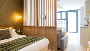 A hotel room with a bed, a wooden partition, a sofa, and a view of the outside.