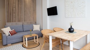 A modern living room with a grey sofa, a small wooden table, wicker chairs, a round rug, and a wall-mounted TV.