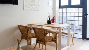 A modern living room with a dining area, featuring a flat-screen TV, a large abstract painting, a fire extinguisher, and a large window with a view.