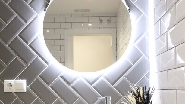 A modern bathroom with a round mirror, white sink, and a decorative vase.