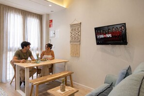 A room with a dining table, two chairs, a TV mounted on the wall, and a sofa. - The Sea Rooms XI | AC & WIFI | 15 min Beach (Valencia)