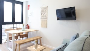 Una sala moderna con televisor montado en la pared, un comedor con sillas de mimbre, una mesa de madera y un sofá.
