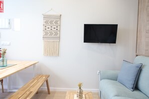 A living room with a light blue sofa, a wooden table with a bench, a wall-mounted TV, and a macramé wall hanging. - The Sea Rooms XI | AC & WIFI | 15 min Beach (Valencia)