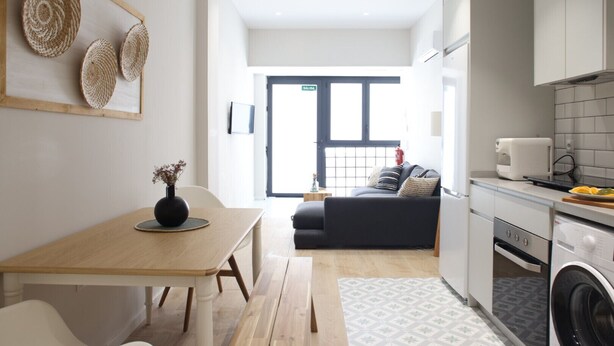A modern kitchen with a washing machine, a dining area with a table and chairs, and a living area with a sofa and cushions. - The Sea Rooms I | AC & WIFI | 15 min Beach (Valencia)
