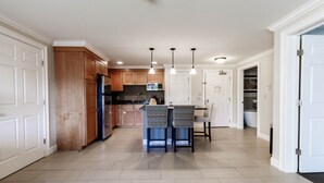 A modern kitchen with wooden cabinets, a central island, pendant lighting, and a view into the dining area.