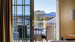 A room with a view of mountains, a balcony with wicker chairs, and a table.