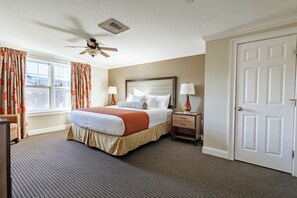 Quarto de hotel com cama, mesas de cabeceira, ventilador de teto, janela com cortinas e porta.