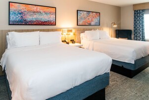 Habitación de hotel con dos camas, una mesita de noche, una lámpara y arte abstracto en las paredes.