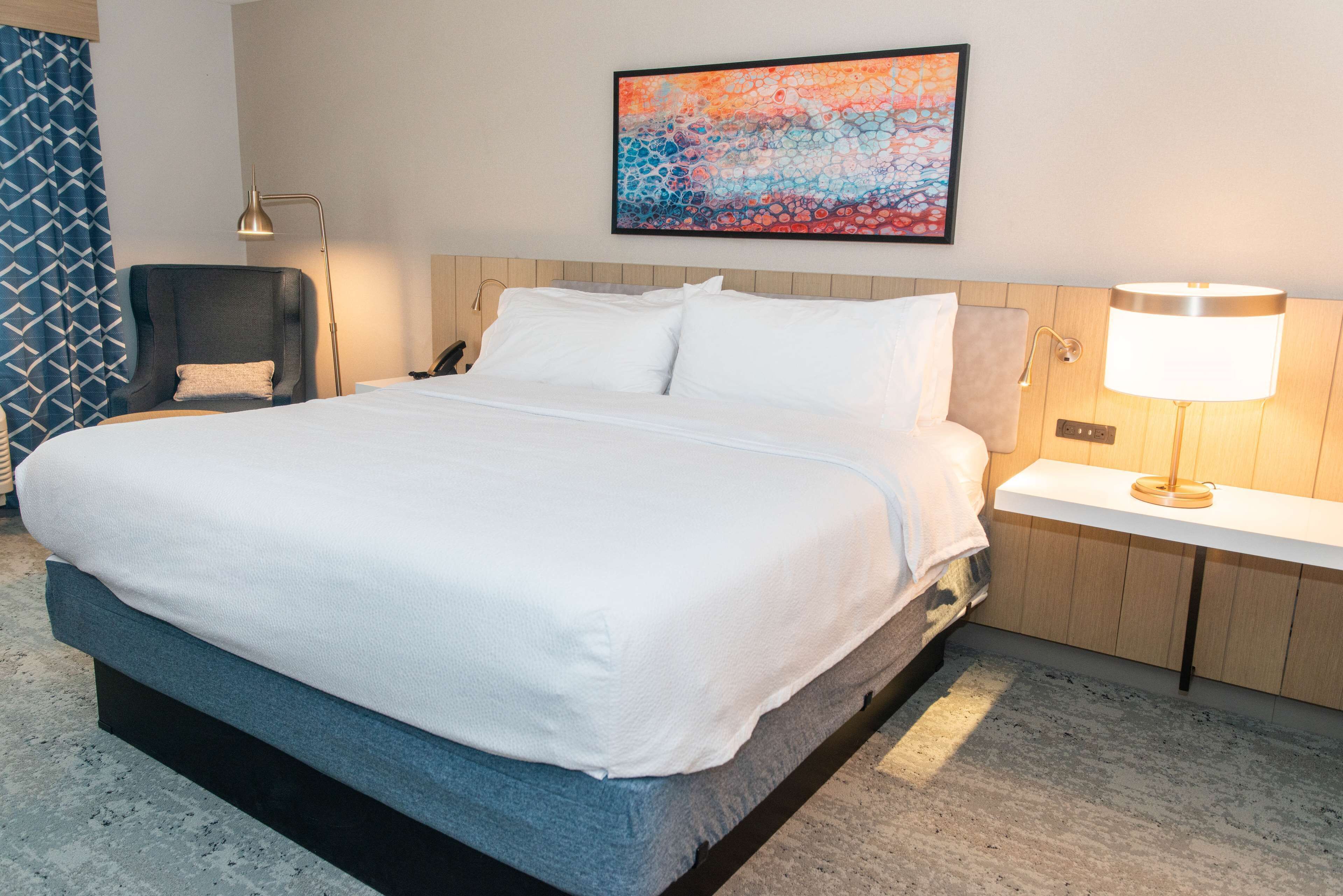 Een hotelkamer met een groot bed, een stoel, een bureau en een schilderij aan de muur.