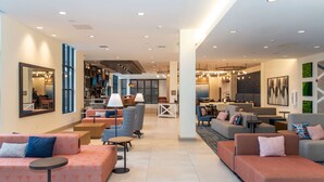 Eine großzügige Lobby mit modernen Sitzbereichen, einer zentralen Kaffeestation und einer sichtbaren Küchenzeile.