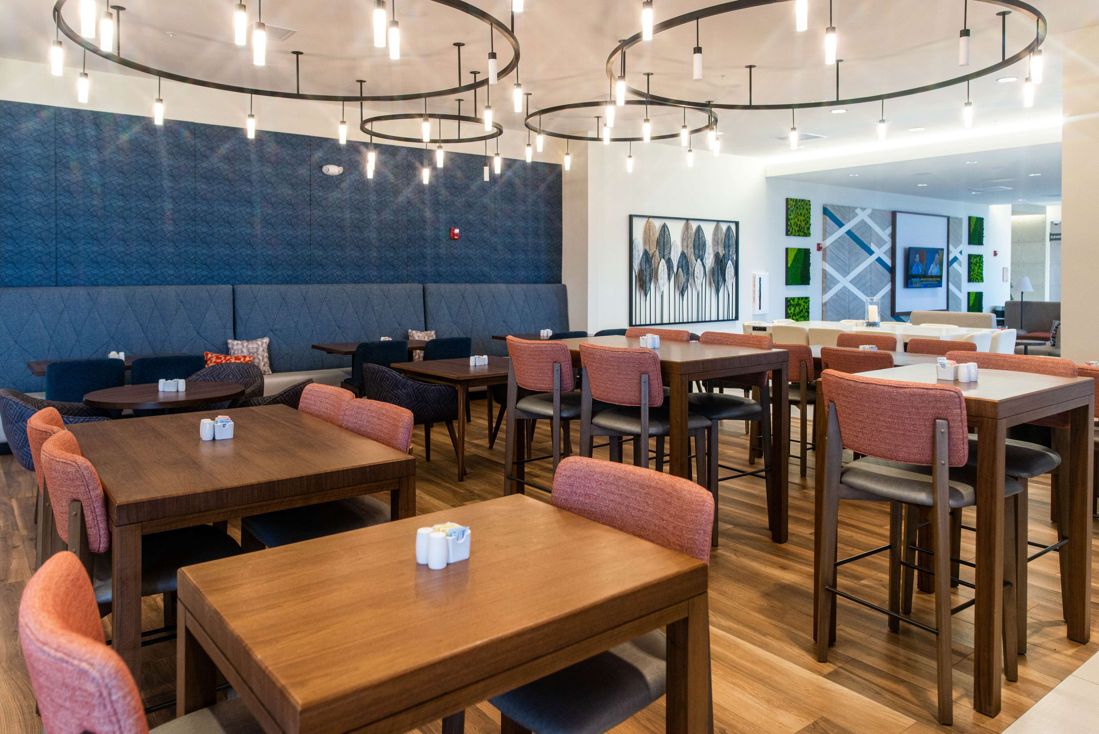 En moderne restaurant med træborde og -stole, en blå accentvæg og et moderne loftslampesæt.