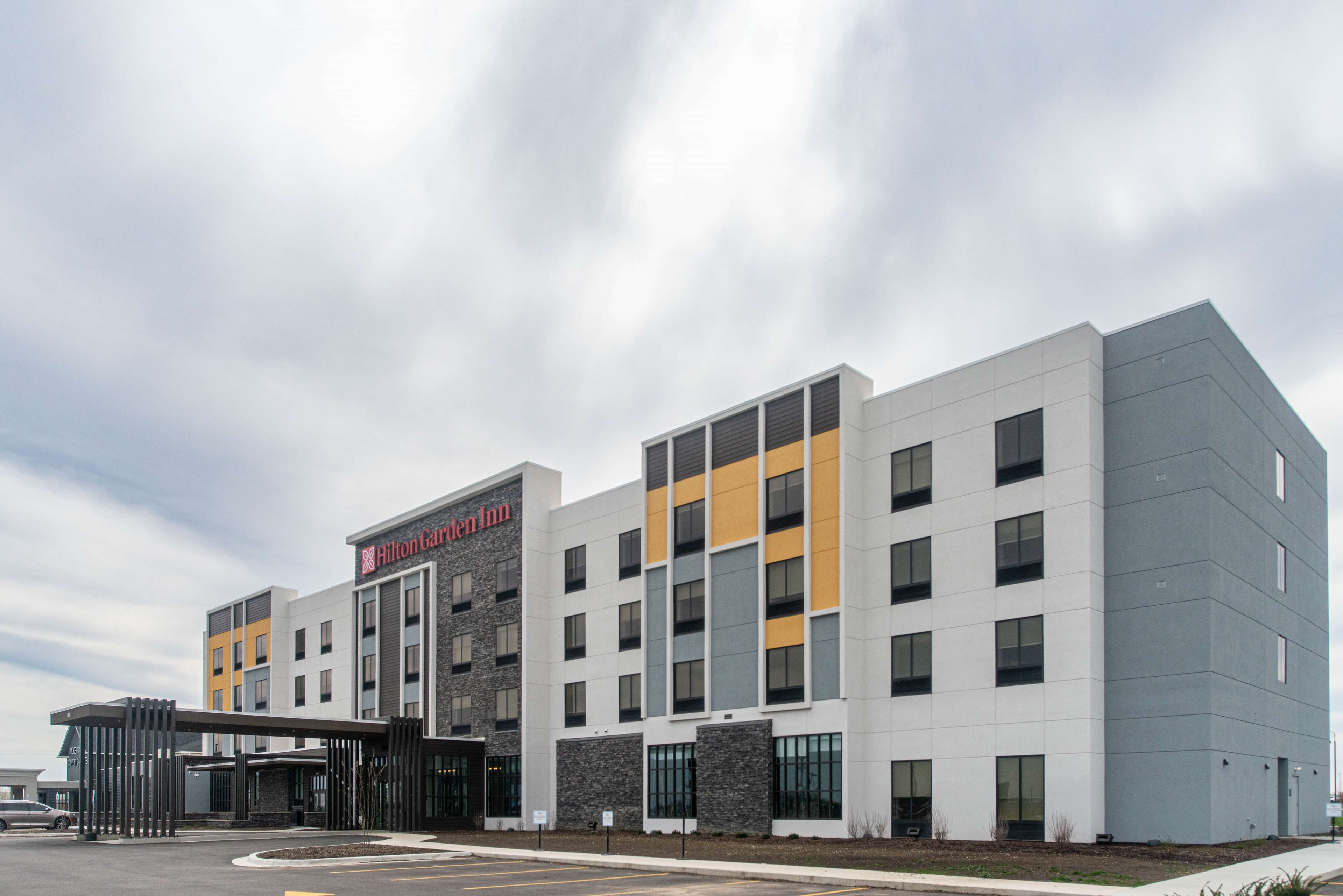 A modern hotel with a prominent 'Hilton Garden Inn' sign, a covered entrance, and a parking lot.