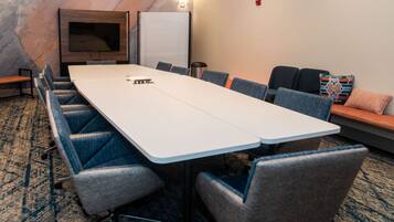 A conference room with a long table, blue upholstered chairs, a flat-screen TV, and a whiteboard.