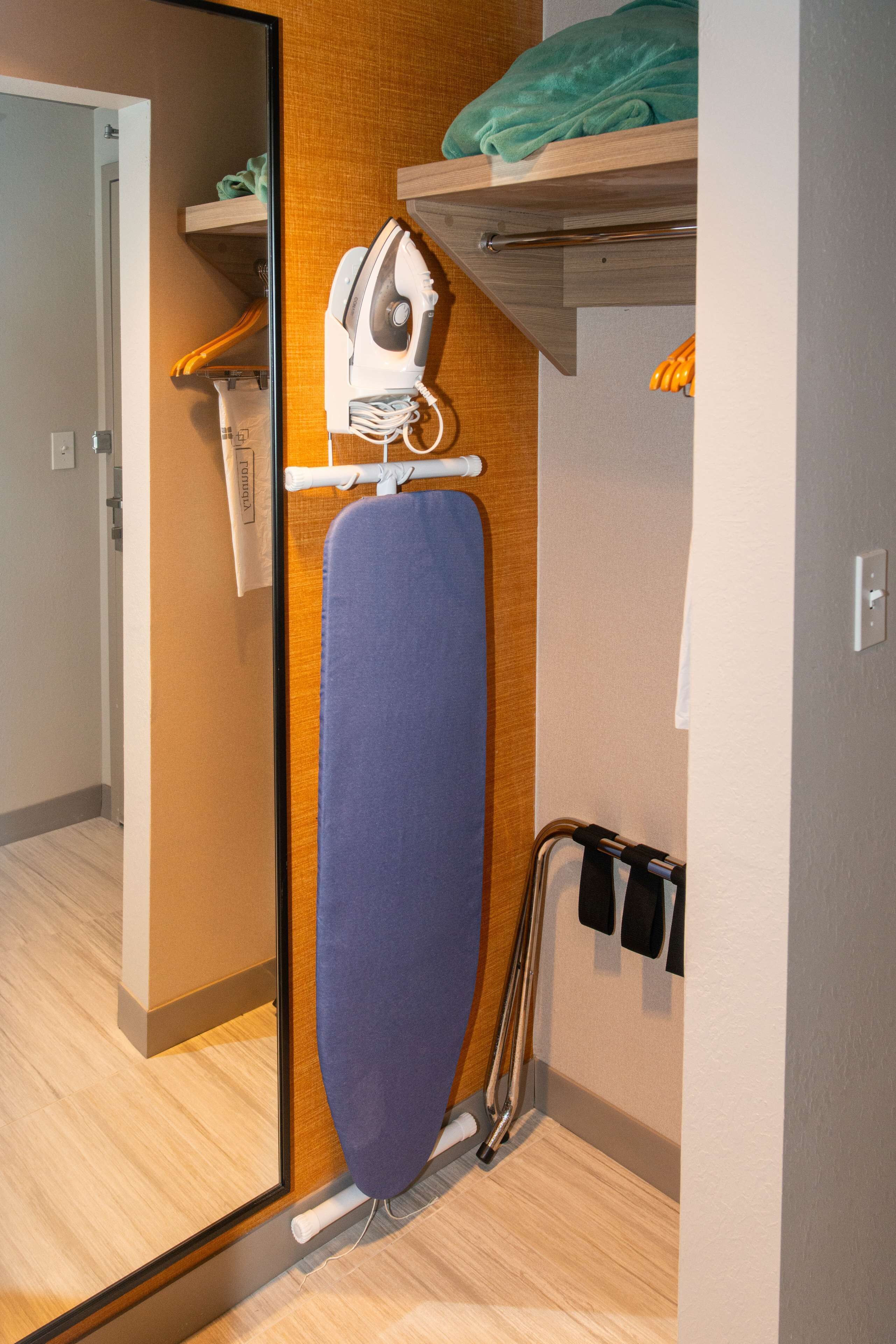 Une pièce de taille modeste, dotée d’un plancher en bois, d’un espace intégré pour repasser et d’un miroir.