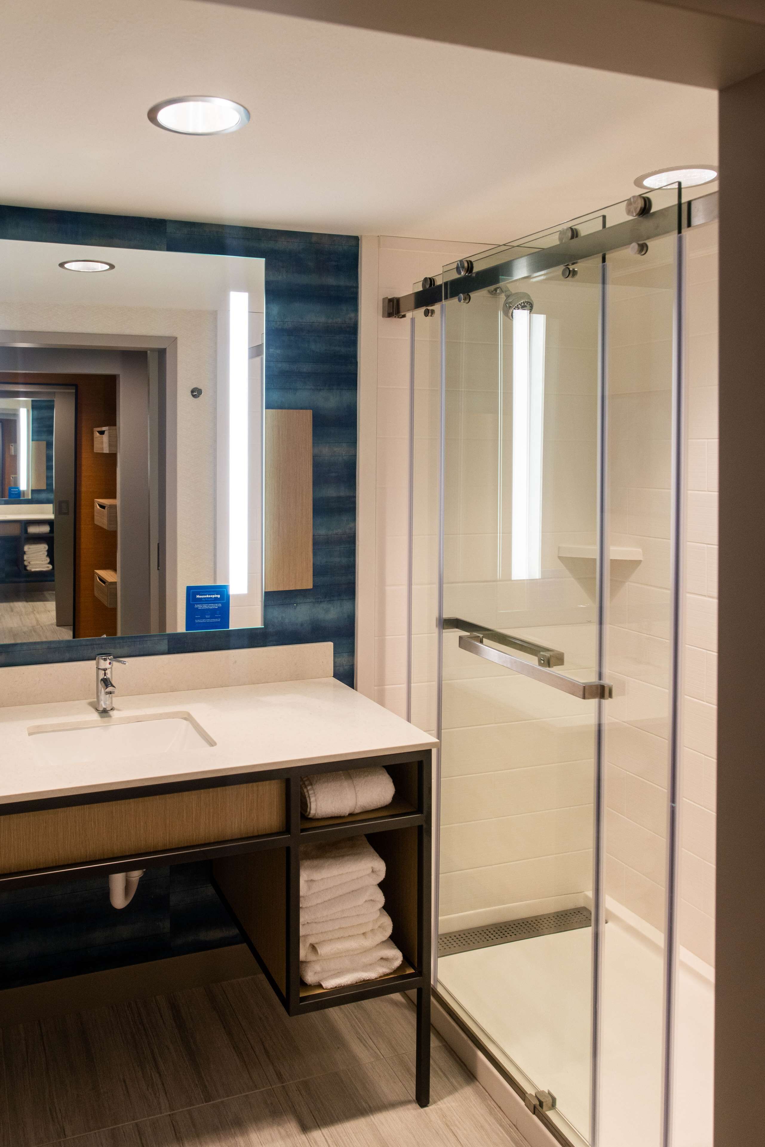 A modern bathroom with a glass-enclosed shower, a large mirror, and a sink with a towel rack.