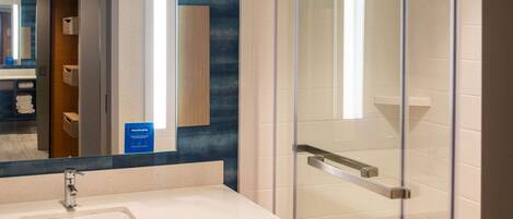 A modern bathroom with a glass-enclosed shower, a large mirror, and a sink with a towel rack.