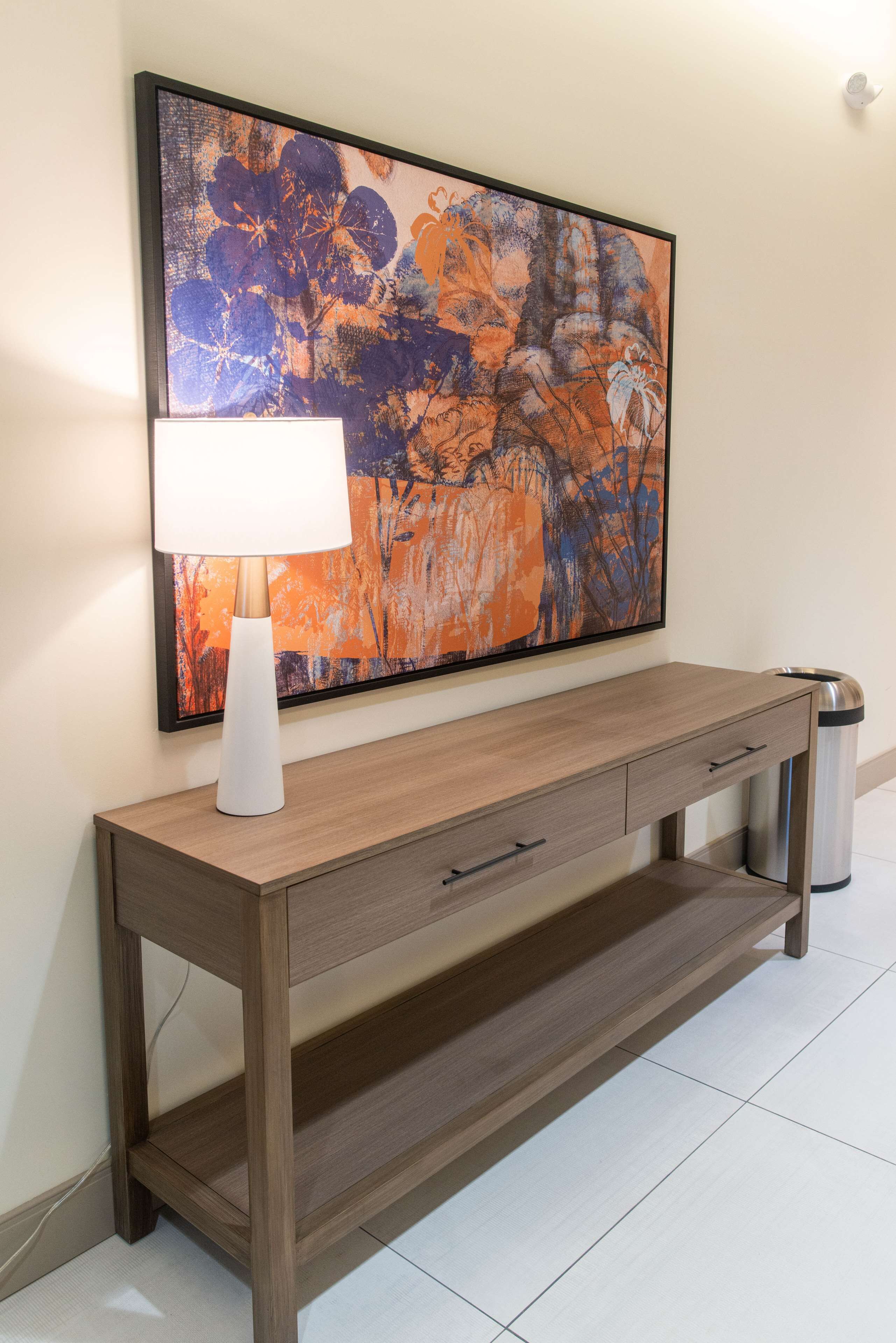 Una consola de madera con una lámpara blanca y un cubo de basura.