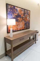 Una consola de madera con una lámpara blanca y un cubo de basura.
