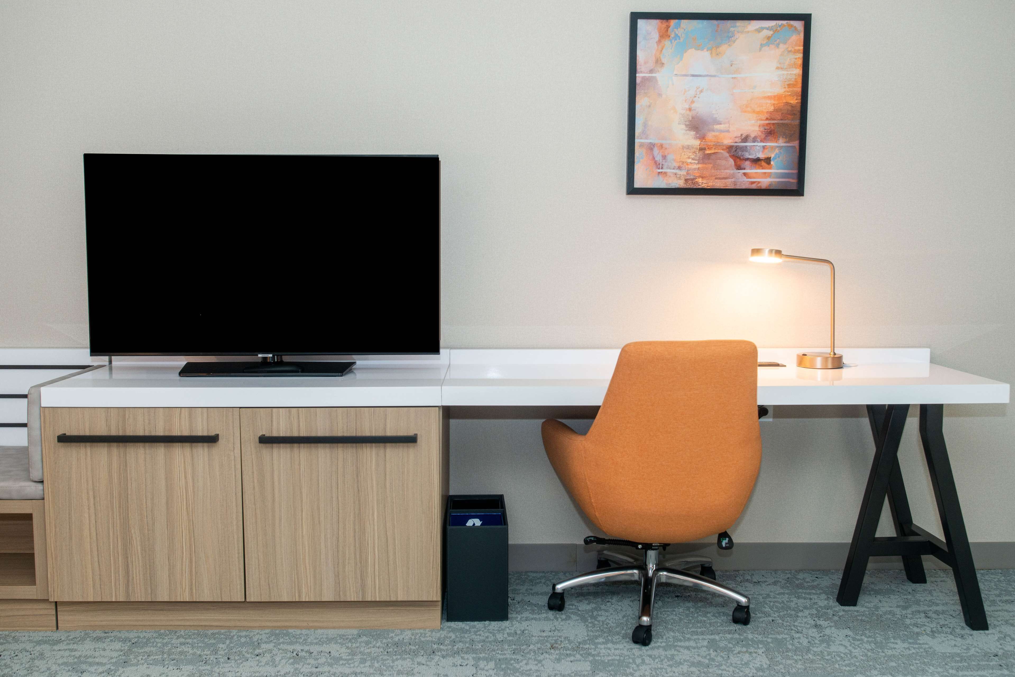 A modern office desk with a flat-screen TV, a desk lamp, and an orange office chair.