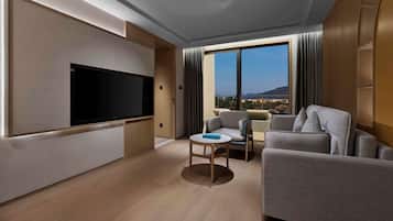Una camera d'albergo moderna con una grande TV a schermo piatto, un divano, un tavolino e un'ampia finestra con vista sulla città.