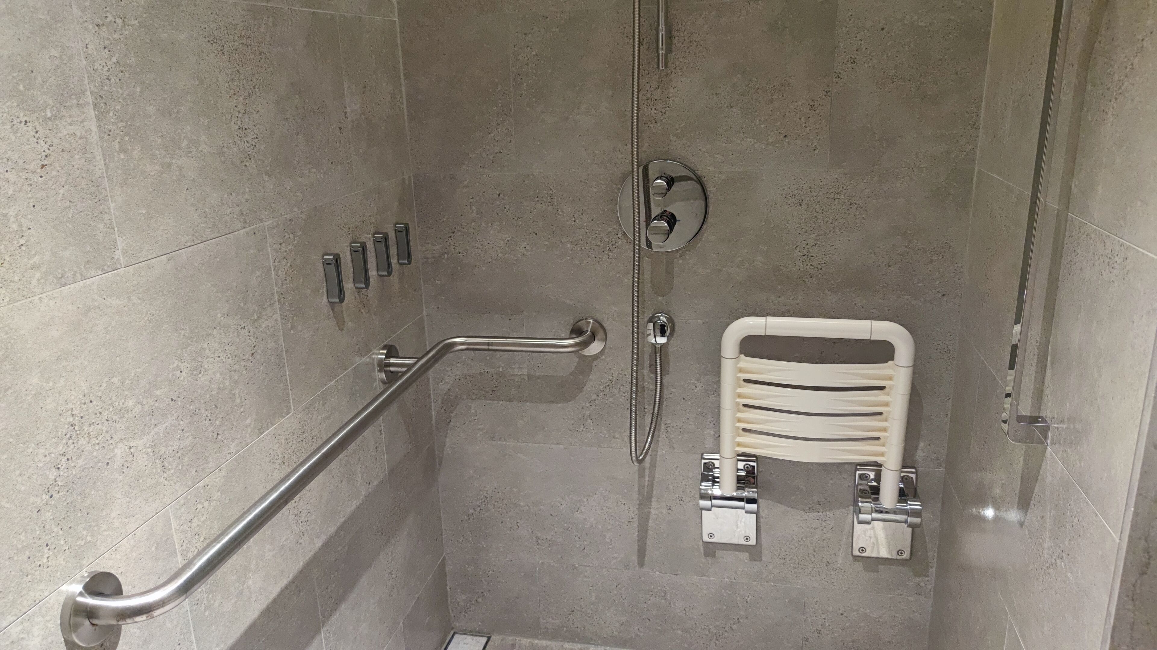 A shower area with a grab bar, a handheld showerhead, and a towel rack.