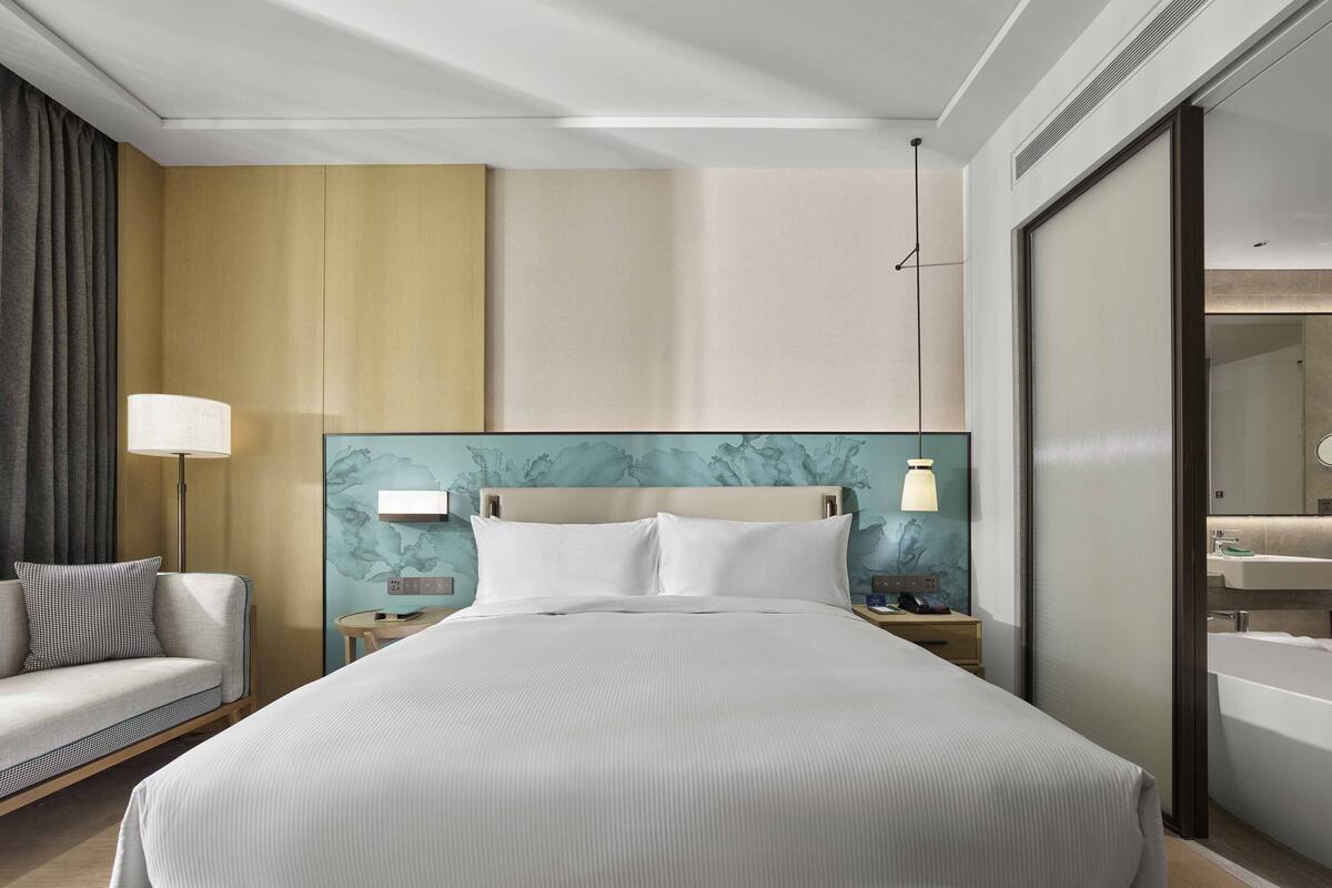 Een hotelkamer met een groot bed, een nachtkastje met een lamp, een kleine zithoek en een badkamer met een bad.