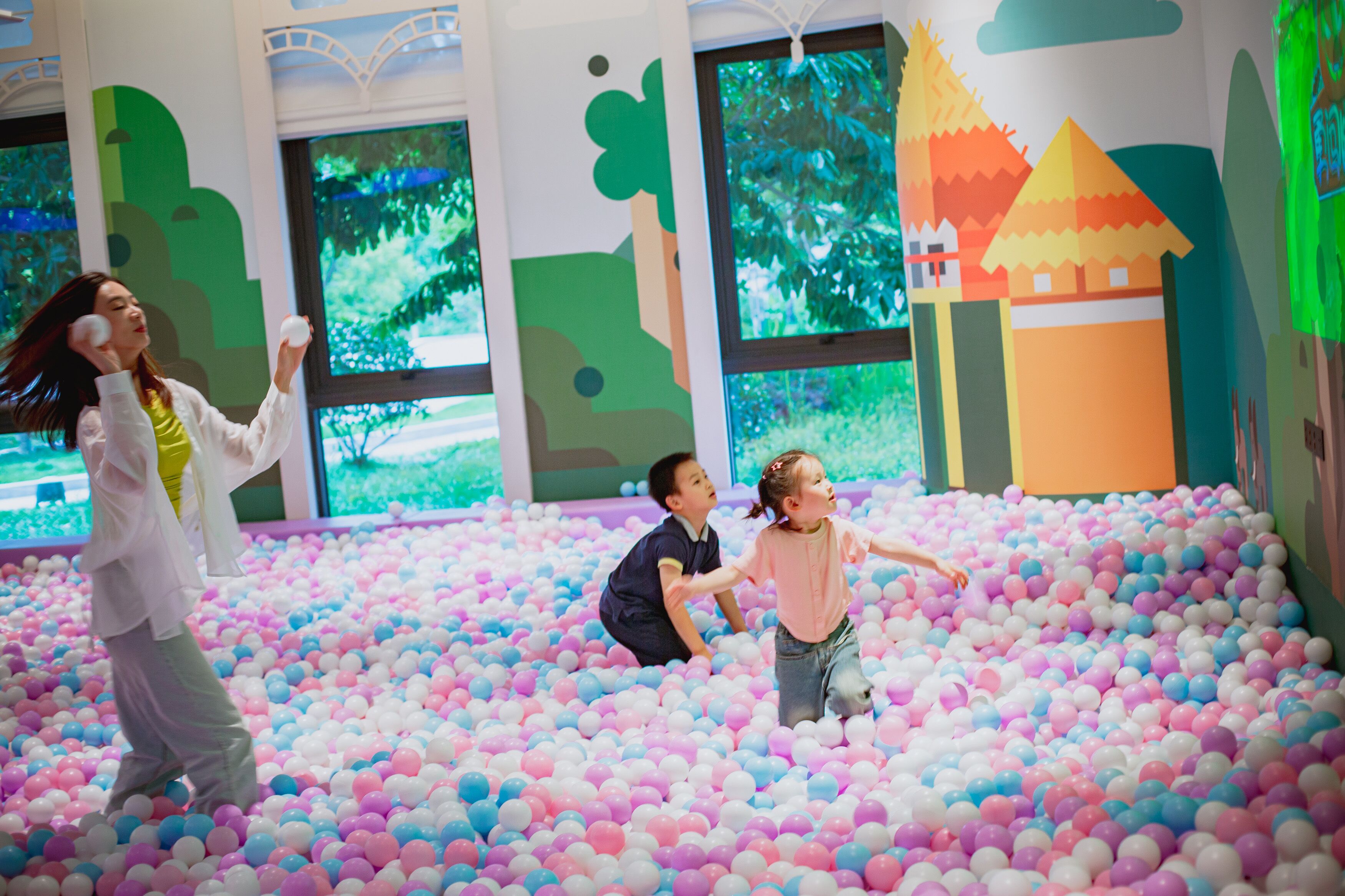 Un área de juegos interior colorida con una piscina de pelotas y ventanas amplias.