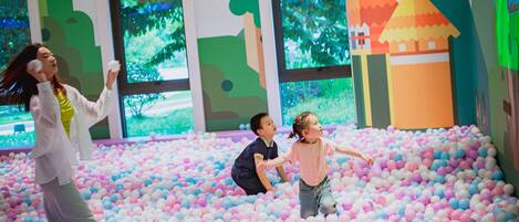 Un área de juegos interior colorida con una piscina de pelotas y ventanas amplias.