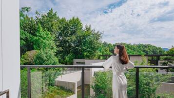 Eine Person steht auf einem Balkon mit Blick auf Grünflächen und Gebäude.