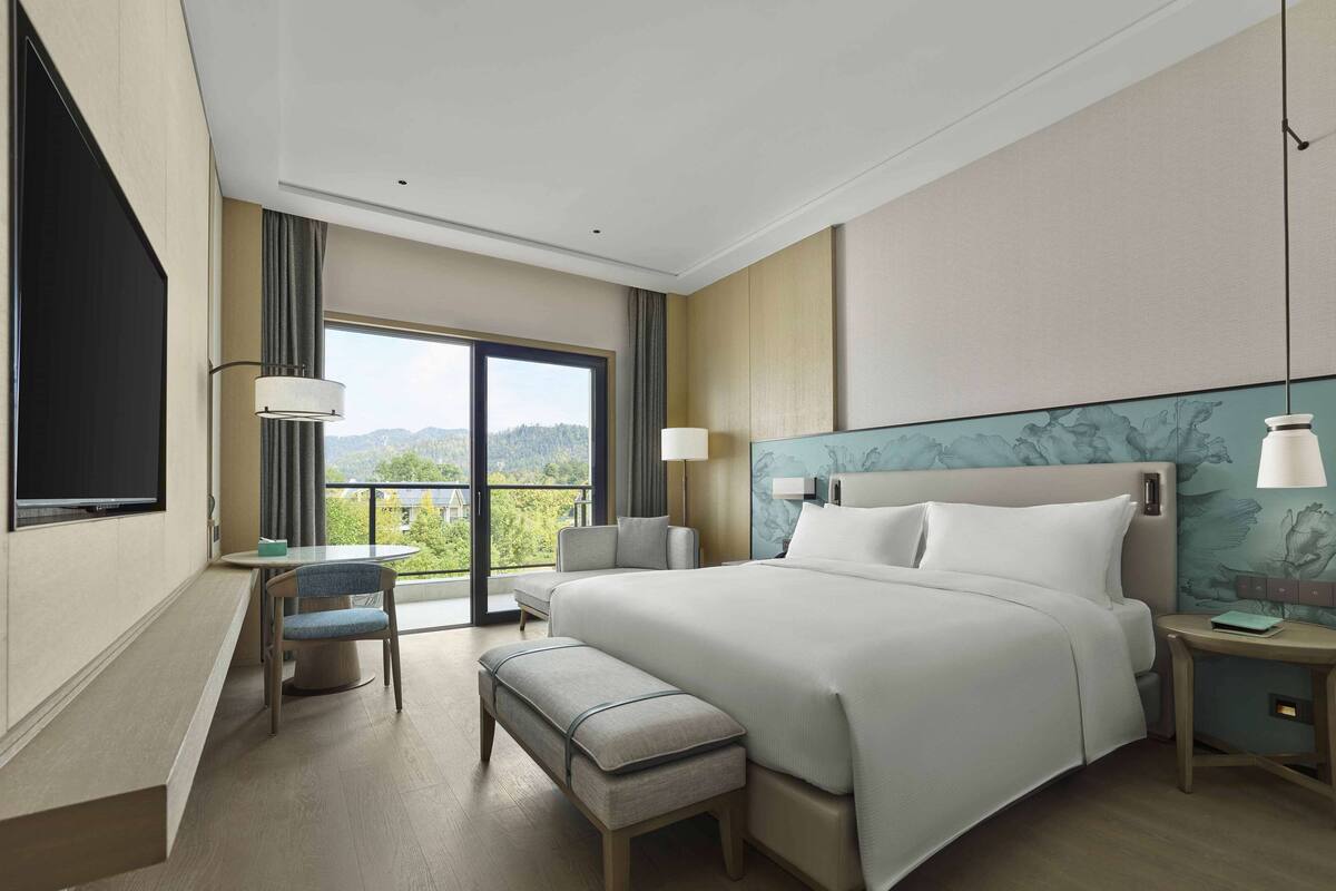 Een moderne hotelkamer met een groot bed, een bureau, een stoel en een balkon met uitzicht op de bergen.