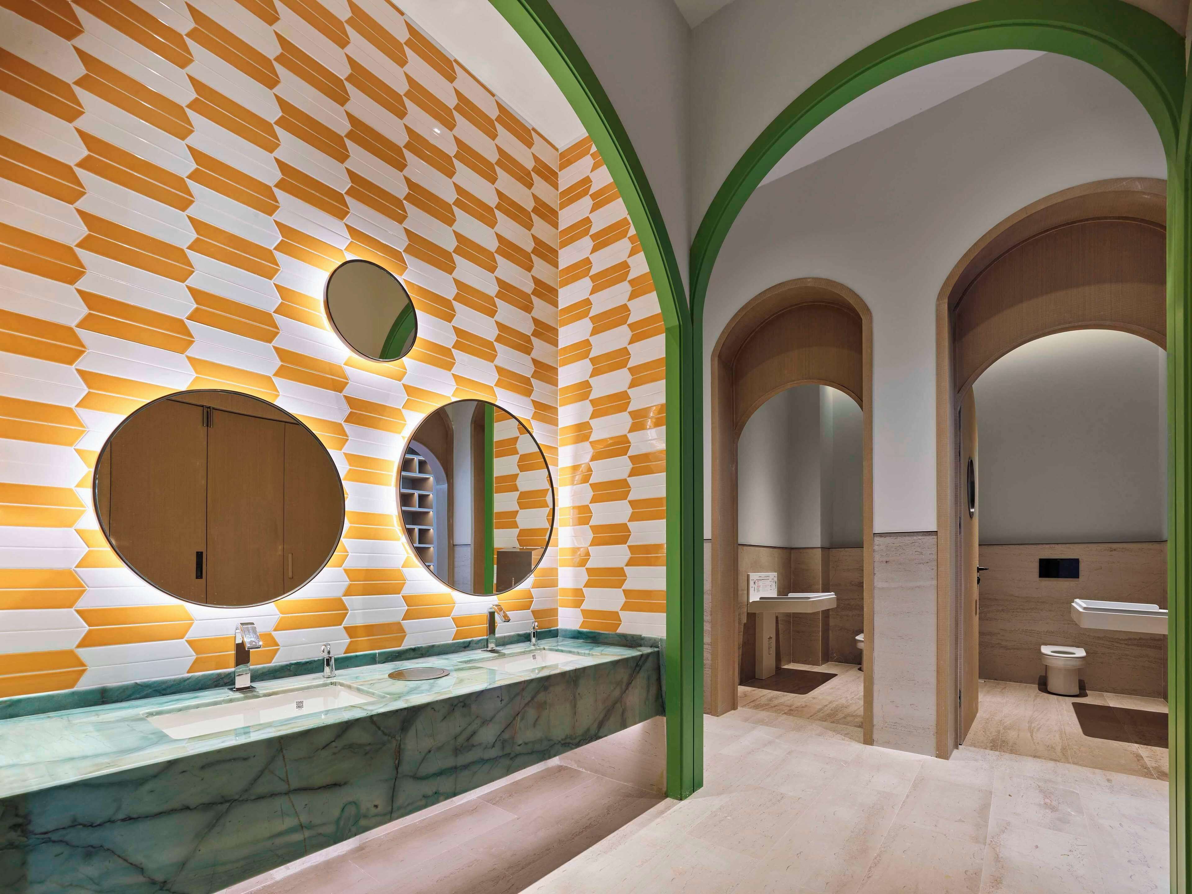 Un baño moderno con pared de diseño geométrico, lavamanos de mármol y varios espejos.