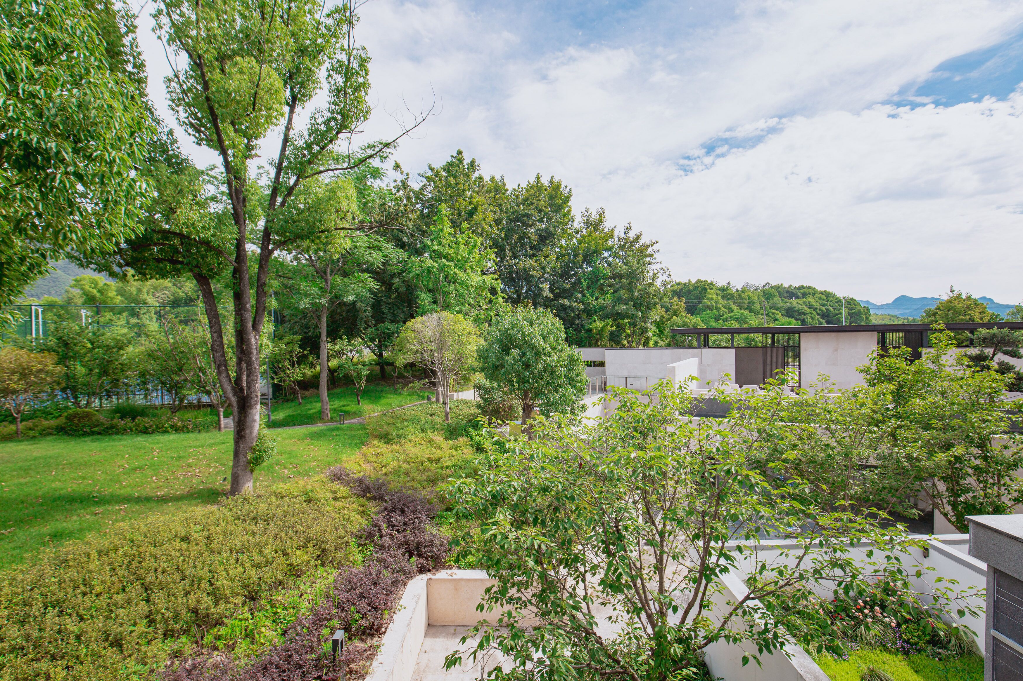 A modern building with a flat roof, surrounded by a well-maintained garden with various trees and shrubs.