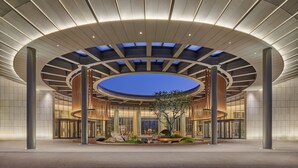 Entrada de un hotel moderno con un tragaluz circular, un atrio central y un jardín ajardinado.