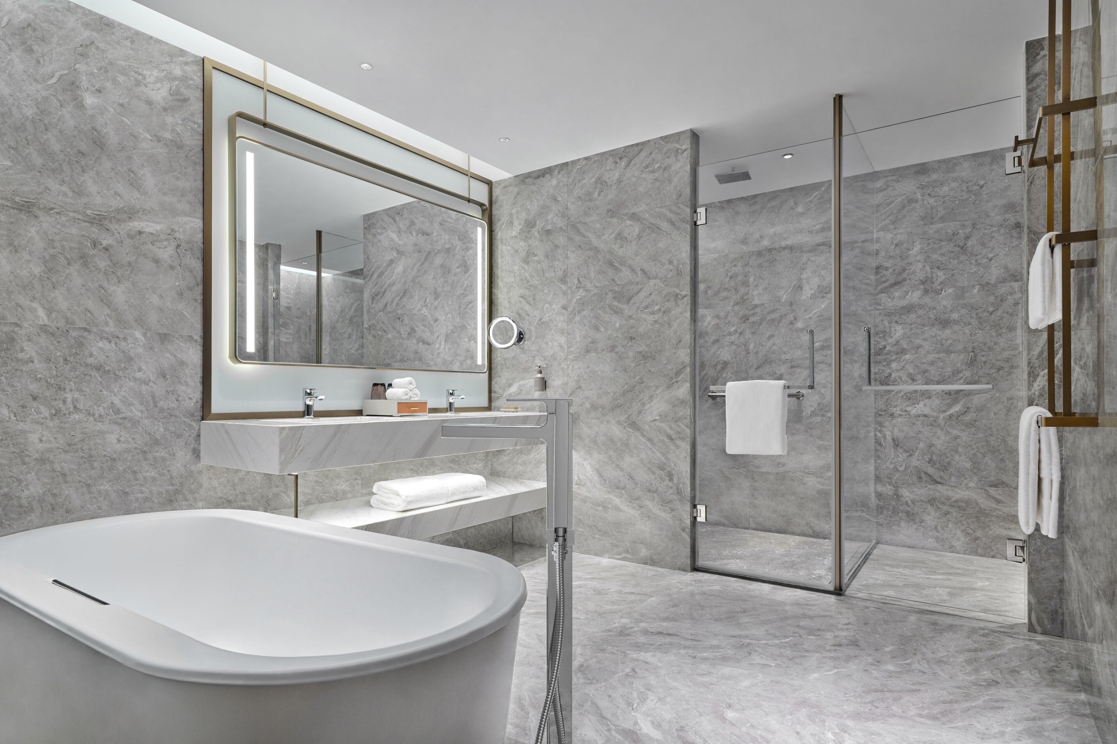 A modern bathroom with a freestanding bathtub, a glass-enclosed shower, and a marble wall.