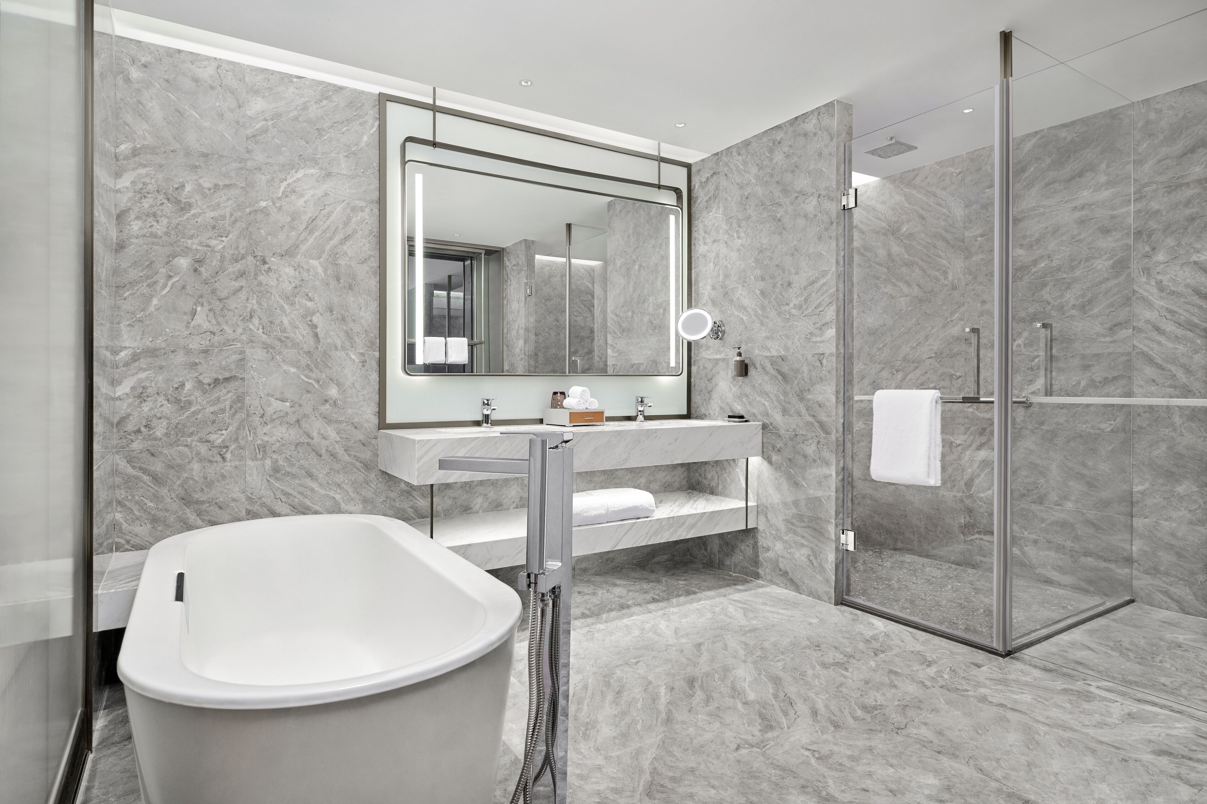 A modern bathroom with a freestanding bathtub, a glass-enclosed shower, and a marble backsplash.