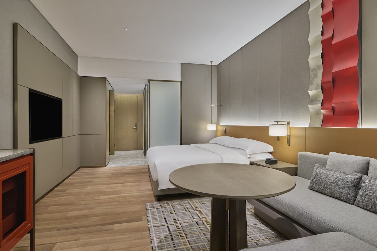 Une chambre d’hôtel moderne équipée d’un lit, d’un canapé, d’une télévision et d’une lampe fixée au mur.