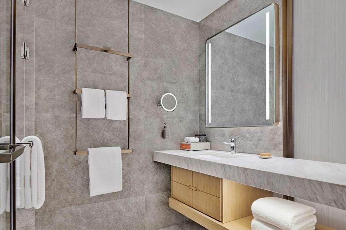 A modern bathroom with a marble sink, wooden vanity, and a large mirror.