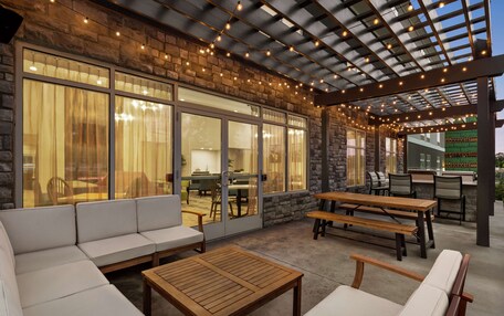 An outdoor patio with stone walls, large windows, and wooden furniture.