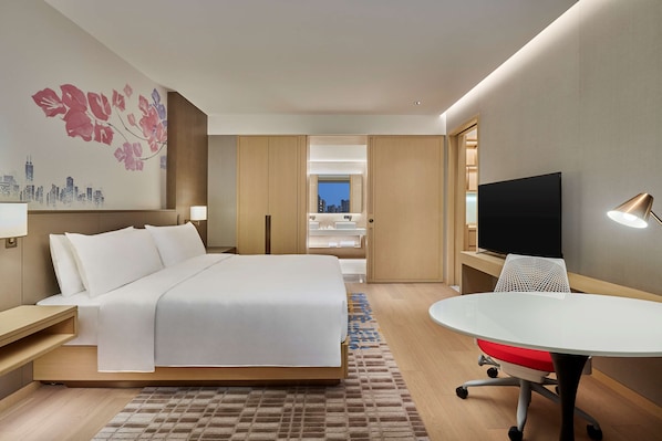A modern hotel room with a large bed, a desk with a TV, and a view of the cityscape through a window. - Hilton Garden Inn Shenzhen Guangming (Shenzhen)