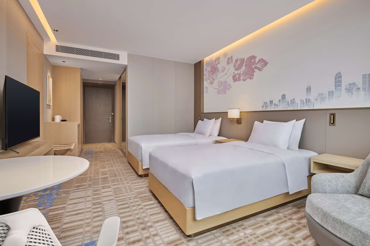 A hotel room with two beds, a TV, a desk, and a chair.