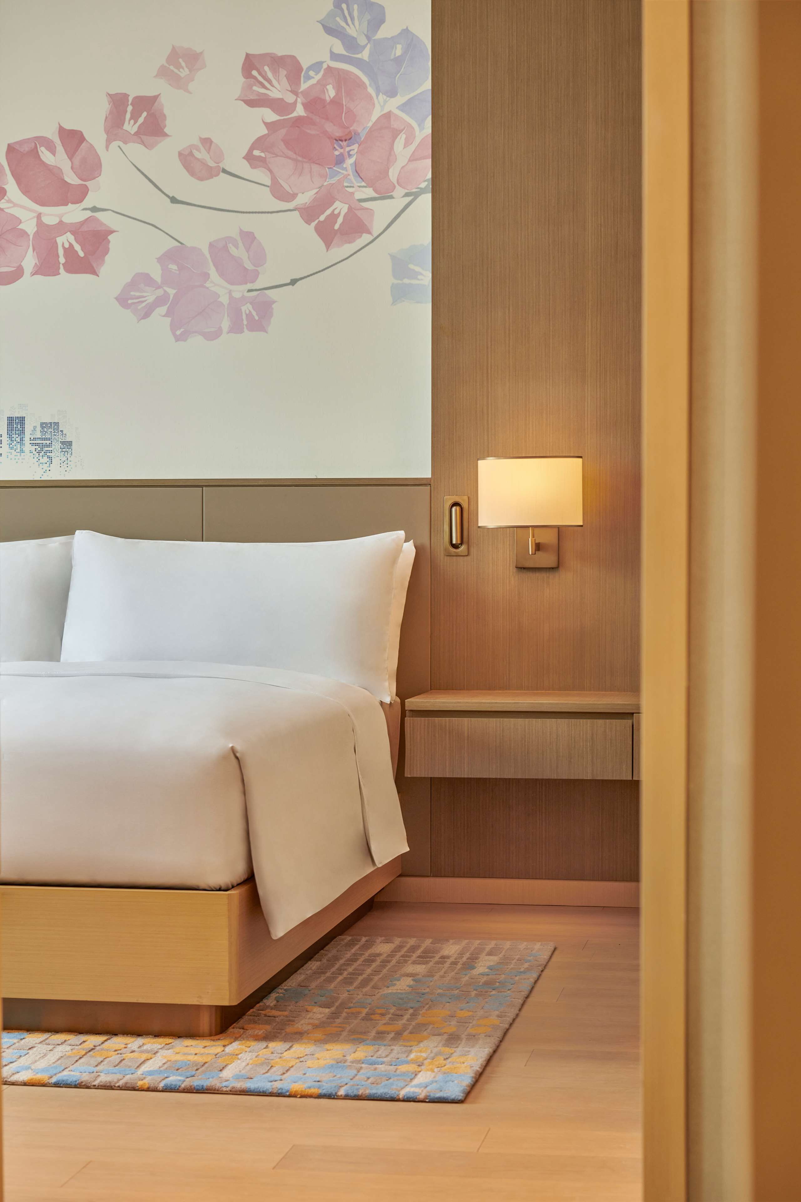 Una habitación de hotel con una cama, una lámpara de pared y una alfombra estampada.