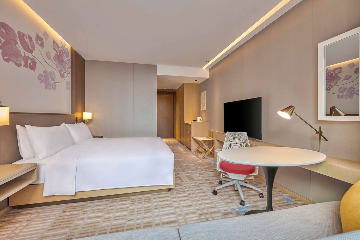 A hotel room with a bed, a desk, a chair, a TV, and a lamp.