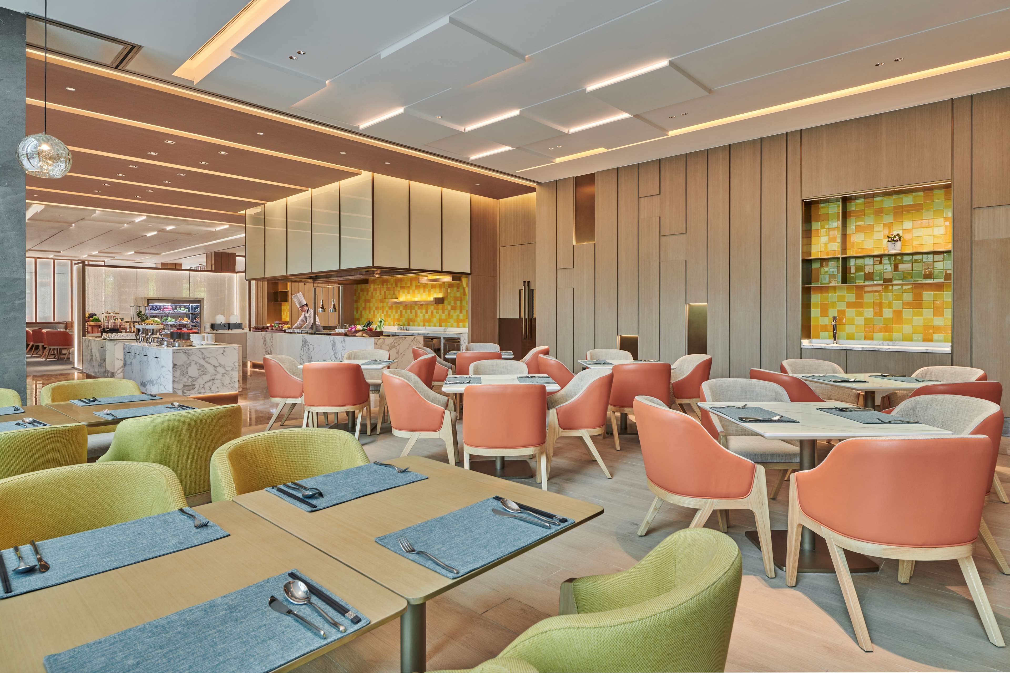 A modern restaurant with a variety of seating options, including tables and chairs, and a visible kitchen area in the background.