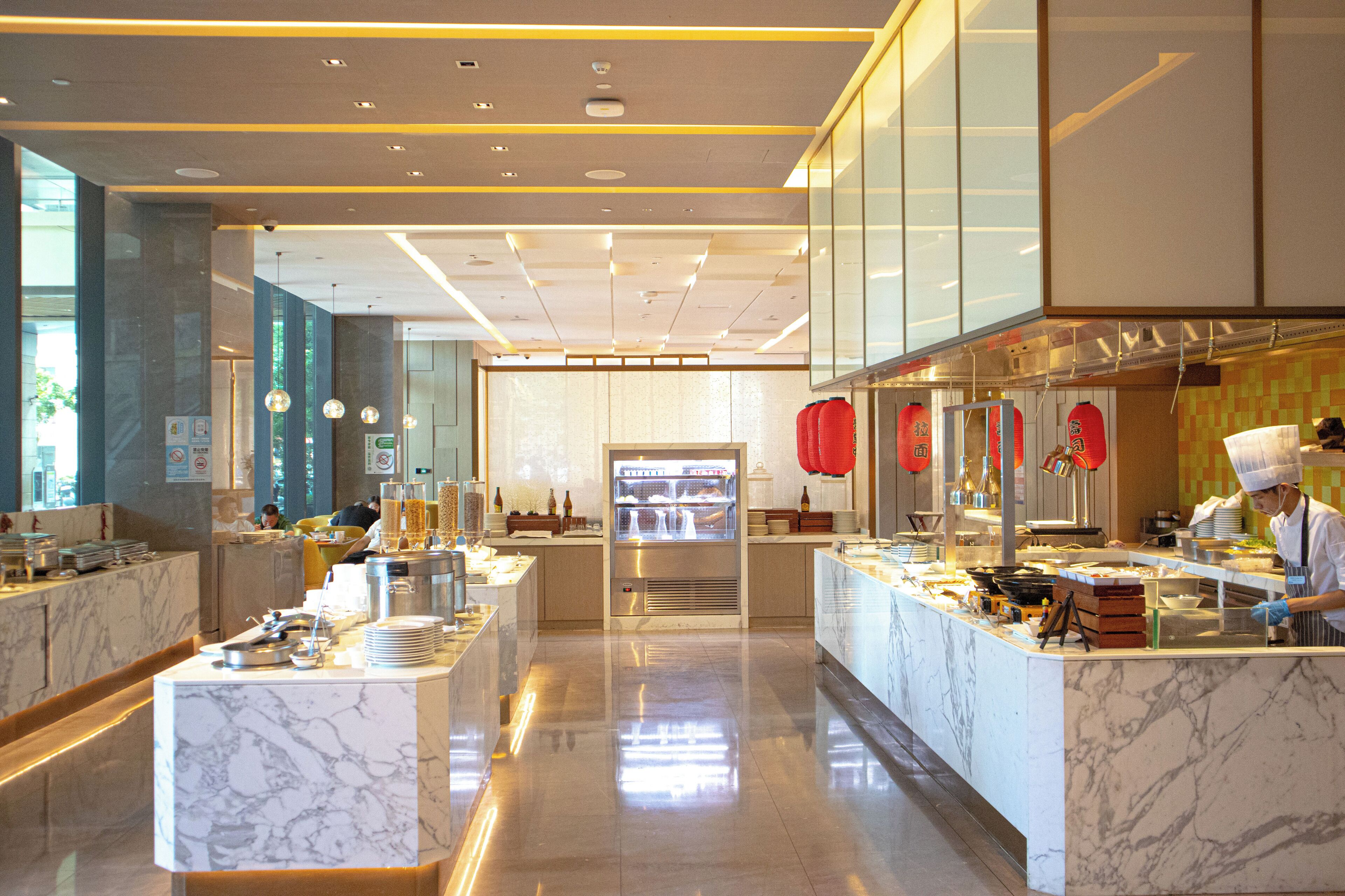 Una cocina de hotel moderna con encimeras de mármol, un mostrador central y un chef preparando comida.
