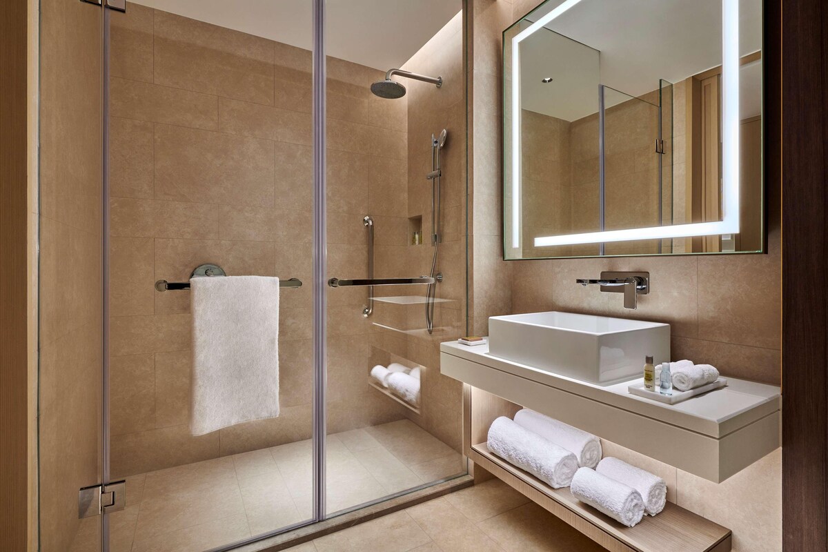 A modern bathroom with a glass-enclosed shower, a white sink, and a large mirror.