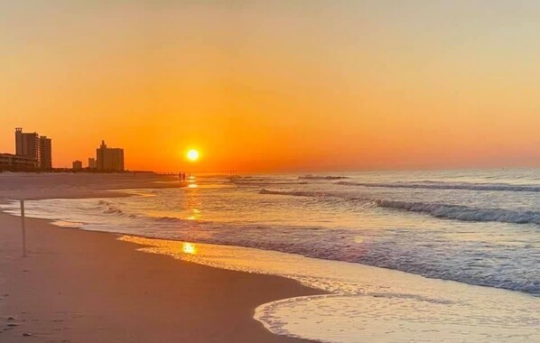 A beach with a sunset, ocean waves, and buildings in the background. - Beautifully renovated 3BR townhome with boat slip just steps from the beach! (Pensacola Beach)