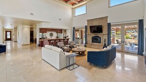 A spacious living area with a fireplace, seating, and a kitchen in the background. - Dresser Winery Estate Villa - Pool, Hot Tub, Sauna on a Vineyard! 10 min to town (Paso Robles)