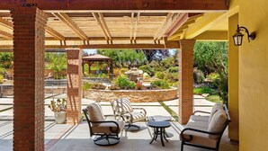 A covered patio with outdoor furniture, a brick pillar, and a view of a landscaped garden. - Dresser Winery Estate Villa - Pool, Hot Tub, Sauna on a Vineyard! 10 min to town (Paso Robles)
